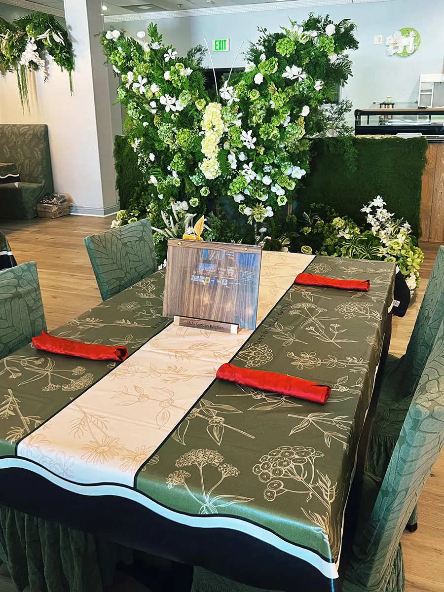 Restaurant dining area with a large floral centerpiece, green chairs, and a botanical-patterned tablecloth at J&J's Garden Kitchen，a Asian Restaurant in Fredericksburg